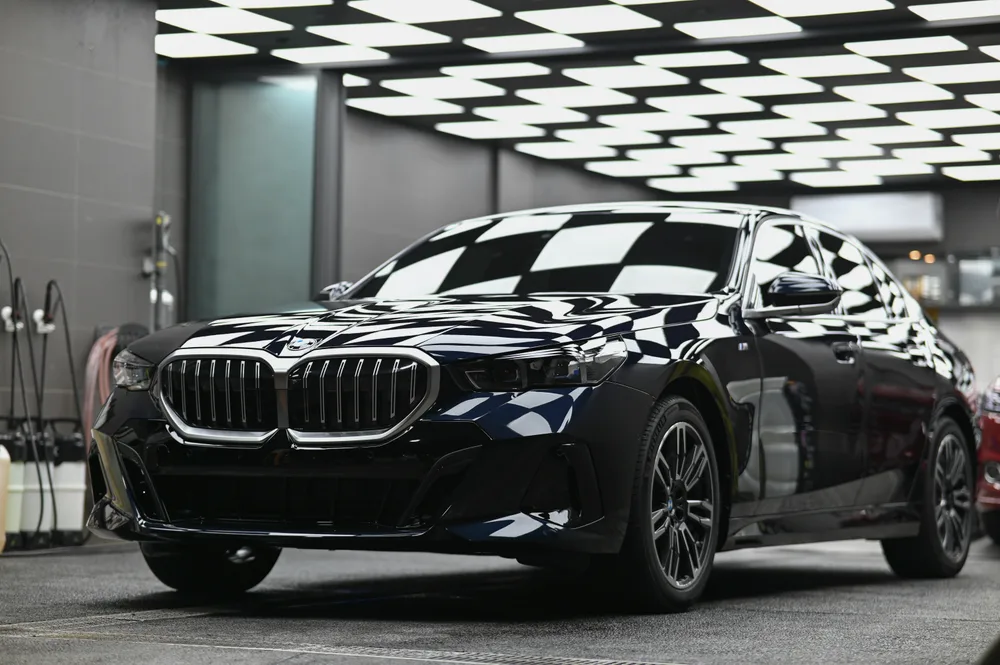BMW 5 系列黑色轎車完工後停在燈箱作業區，車頭 45 度角全車漆面呈鏡面反射｜誠美車體美容