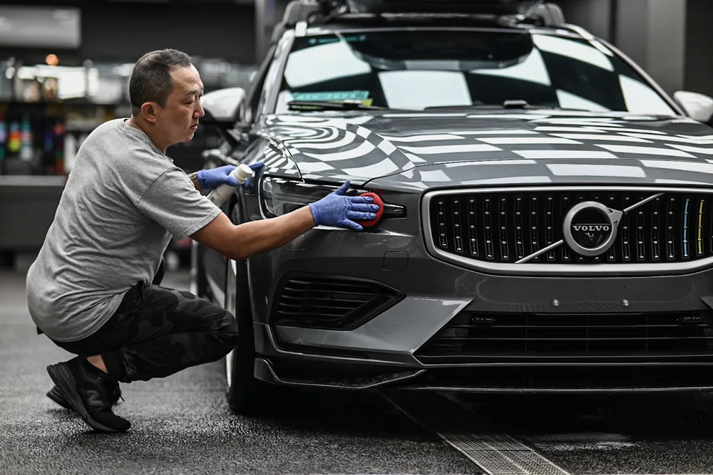 技師蹲在車頭前，逐處清潔水箱罩與前保桿