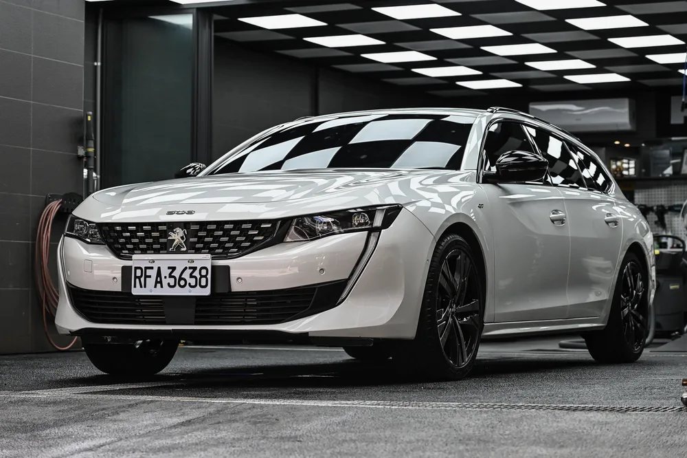 白色 Peugeot 508 SW 完成外觀護理後停於格紋施工區，左前方全景鈑面光澤均勻，誠美車體美容