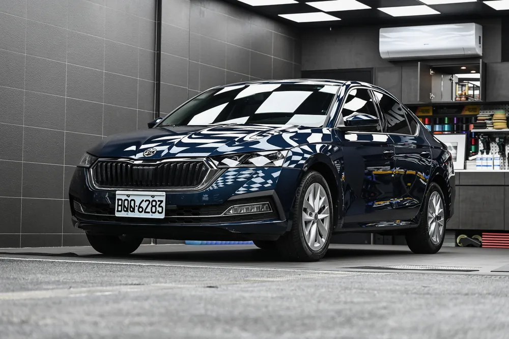 深藍色 Škoda Octavia 完工停放於施工區，車身漆面映出天花棋盤格倒影，誠美車體美容