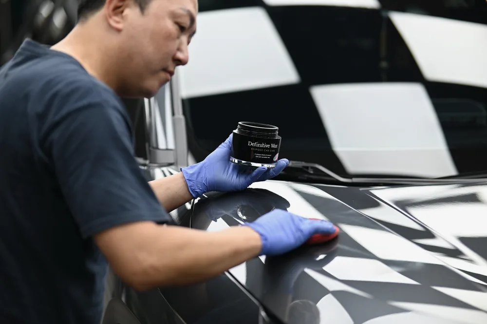技師手持罐裝蠟品，以海綿在車尾鈑面分區塗佈