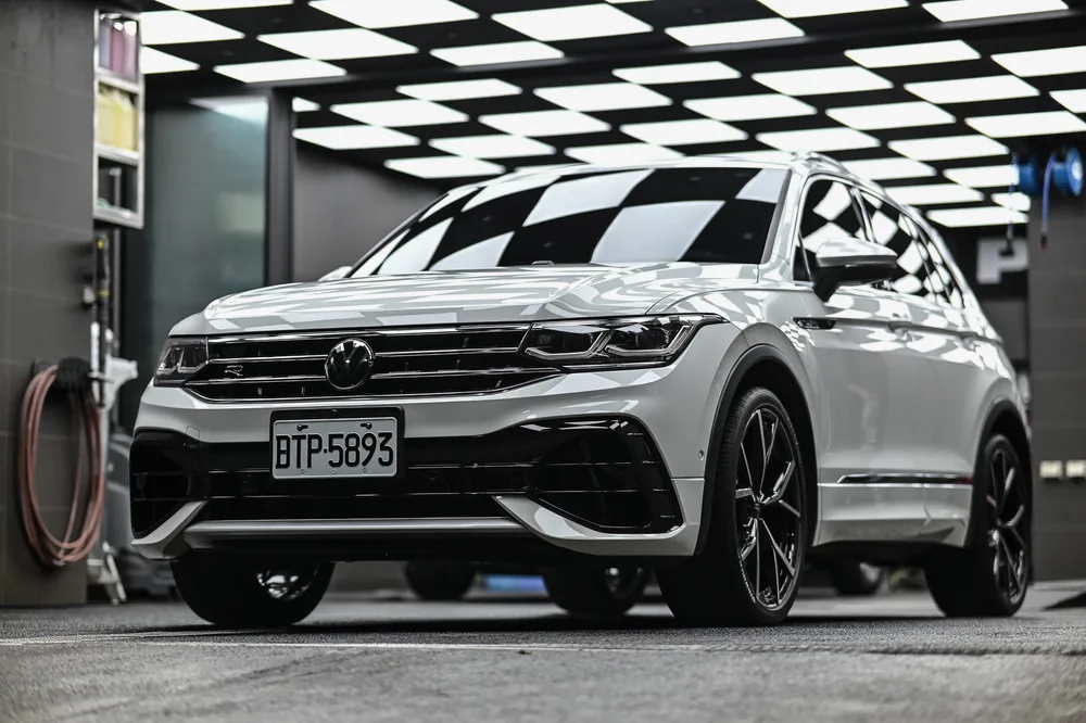 白色 Volkswagen Tiguan 完成精緻打蠟後停於廠內的車頭四分之三視角，車身側面映出棋盤格燈條｜誠美車體美容