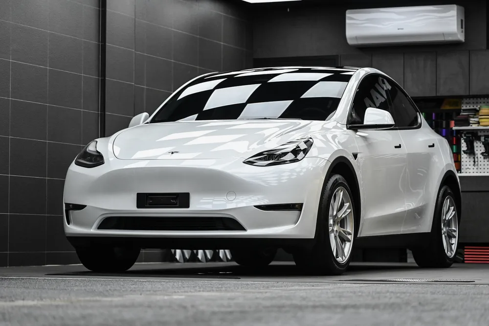 白色 Tesla Model Y 完成雙層鍍膜後，停於施工棚內的左前四十五度車身光澤，誠美車體美容