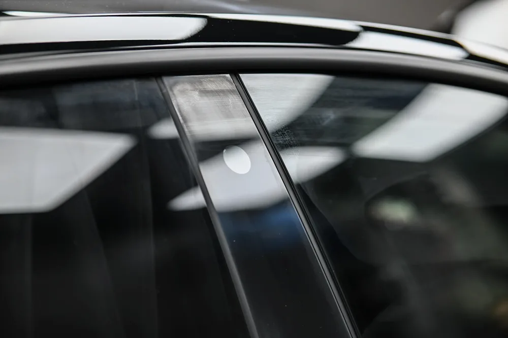完成玻璃拋光鍍膜的黑色 Tesla 車側，前後車窗與 B 柱呈現無霧感的清透倒影，誠美車體美容
