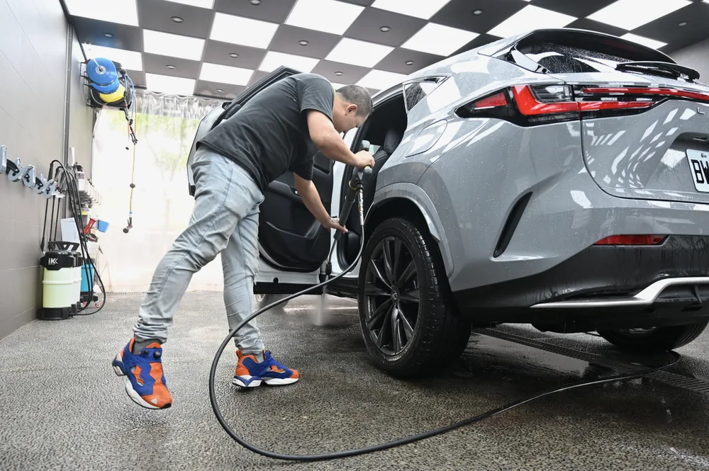 技師以高壓水槍沖洗 Lexus NX 車尾與後保桿，帶走膜面附著的塵砂
