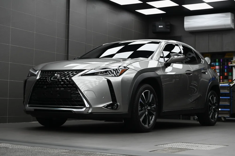 完成雙層鍍膜的銀色 Lexus UX 停在棚拍區，左前方視角車身映出格紋天花板倒影，誠美車體美容