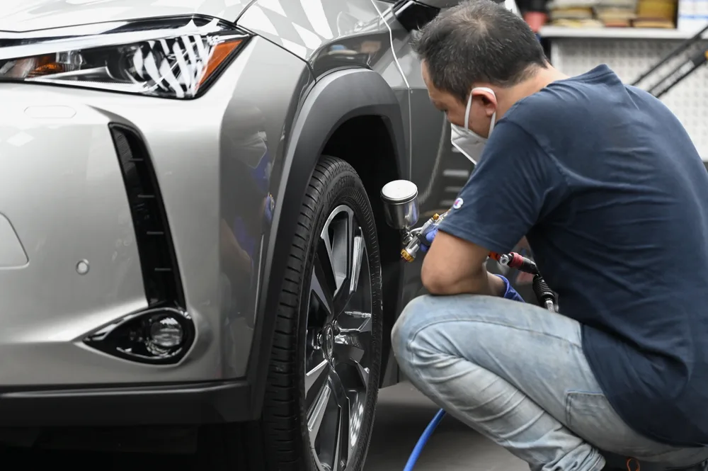 技師蹲在 Lexus UX 前輪旁，手持噴槍為輪圈與輪拱噴塗藥劑