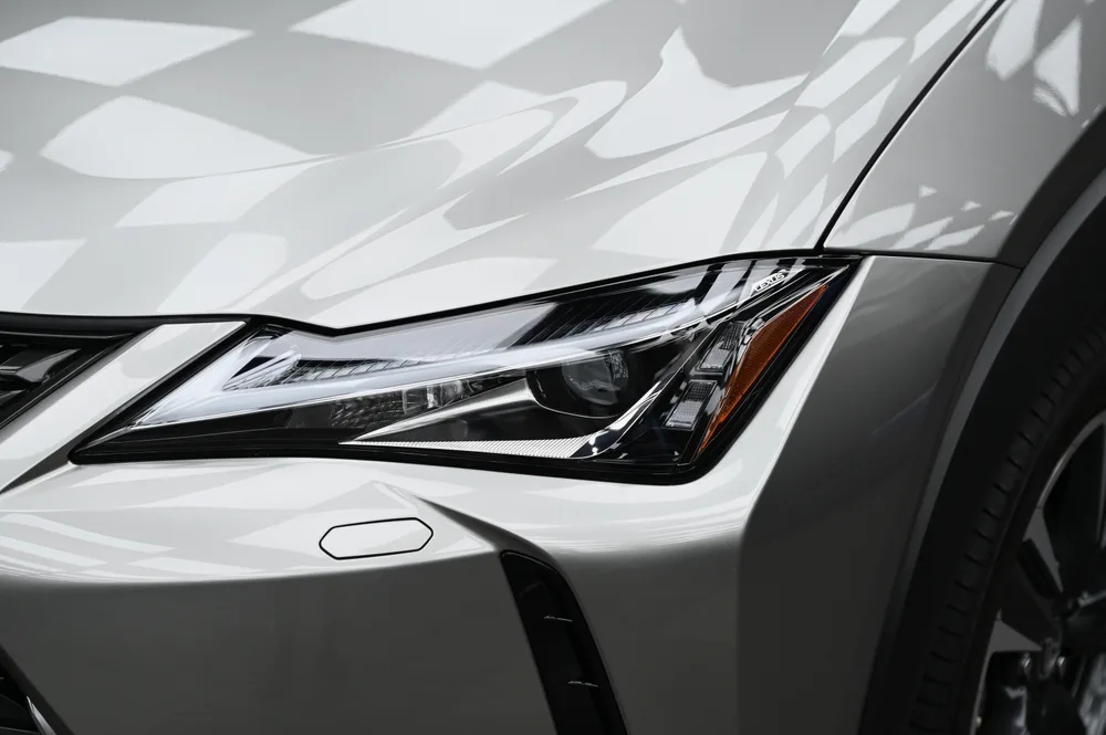 Lexus UX 頭燈與前葉子板特寫，燈組與烤漆表面映出清晰倒影