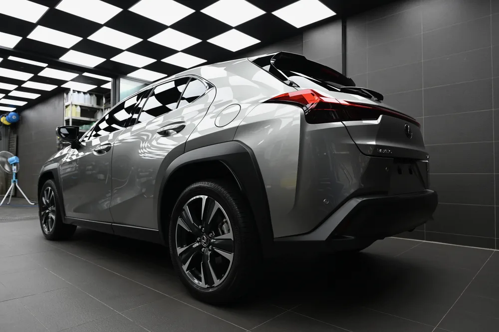 Lexus UX 左後方全景，尾燈與後保桿鈑面在棚拍燈光下呈現鏡面光澤