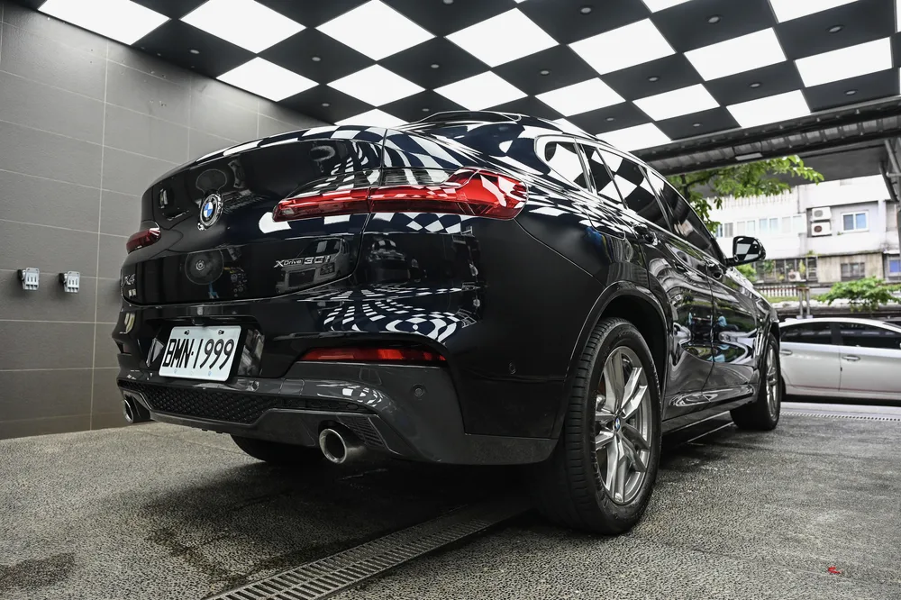 BMW X4 M Sport 左後方全景，尾門與尾管在施工區燈光下呈現光澤