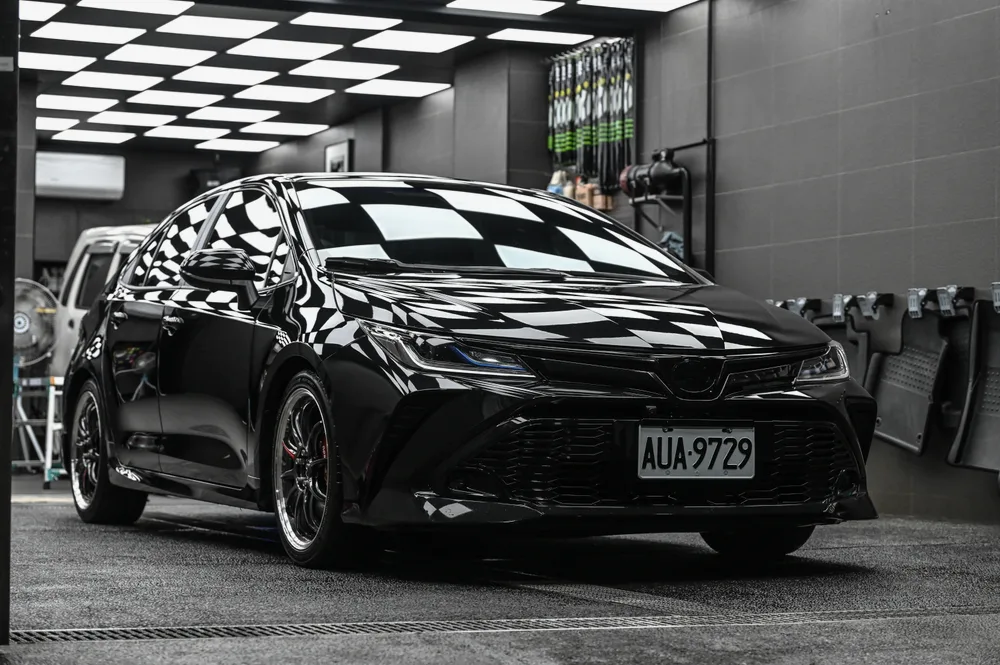 黑色 Toyota 轎車完工後停在棚內，車頭 45 度角漆面映出天花板格紋燈｜誠美車體美容
