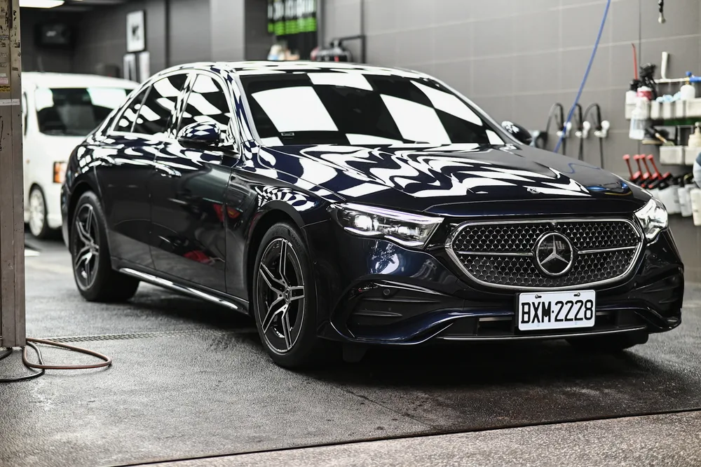 完工後的深藍色 Mercedes-Benz 停在施工區，車頭漆面映出格紋燈光，誠美車體美容