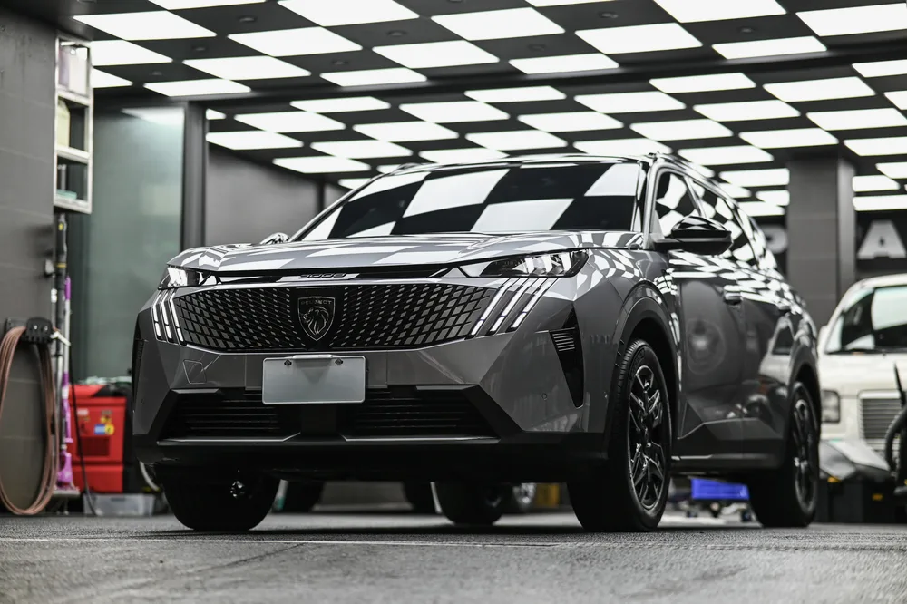 銀灰色 Peugeot 5008 停在施工棚內，車頭正面在黑白格燈光下的整體視角