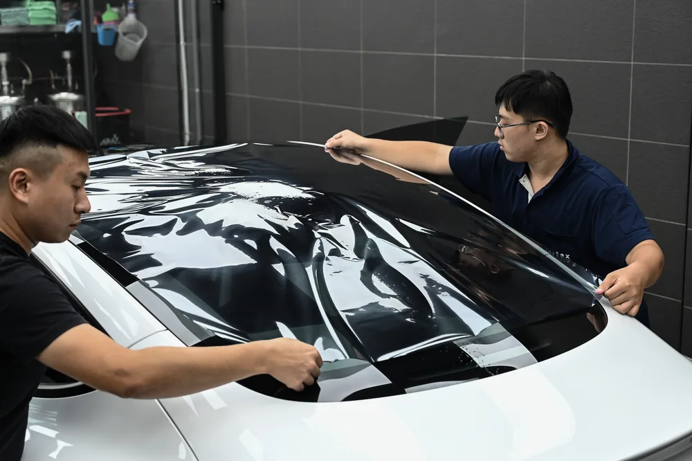 兩名施工人員合力將整片隔熱紙攤平在車頂玻璃上