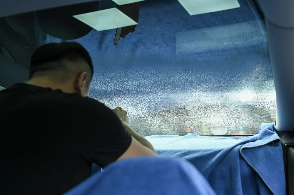自車內視角，施工人員將隔熱紙貼附於前門車窗玻璃
