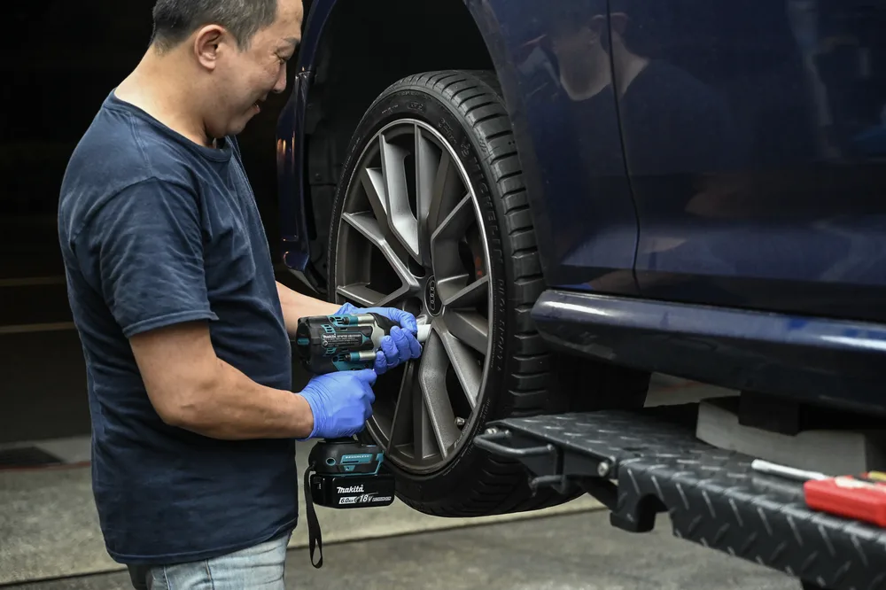 技師手持電動扳手拆卸輪圈，車身以千斤頂架高