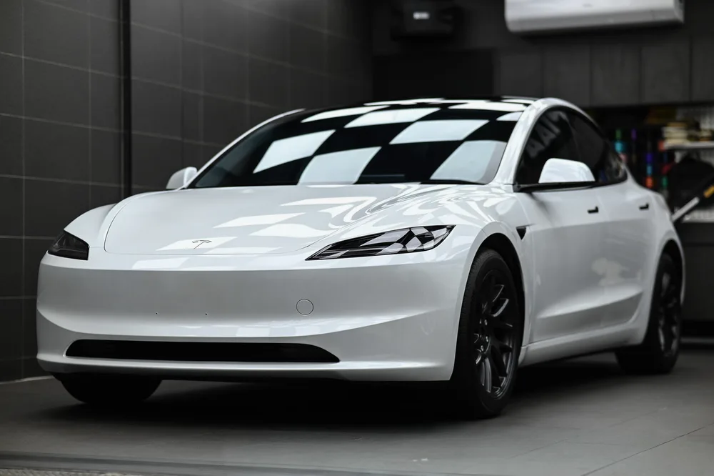 白色 Tesla Model 3 完成拋光與雙層鍍膜後，於施工棚內呈現的左前四十五度車身光澤，誠美車體美容