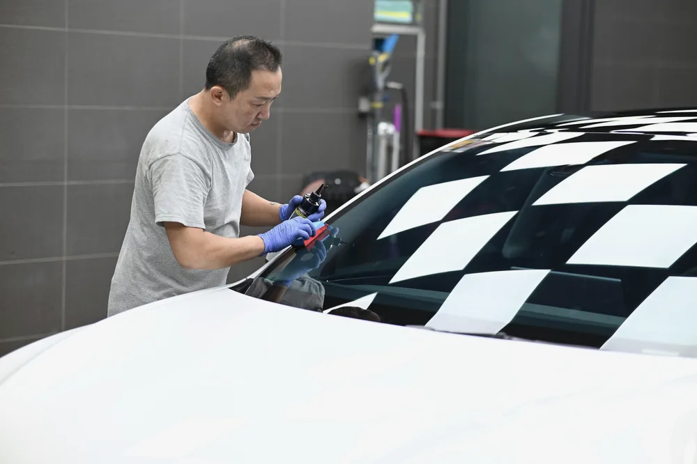 施工人員俯身在前擋風玻璃上以塗抹塊施作玻璃鍍膜