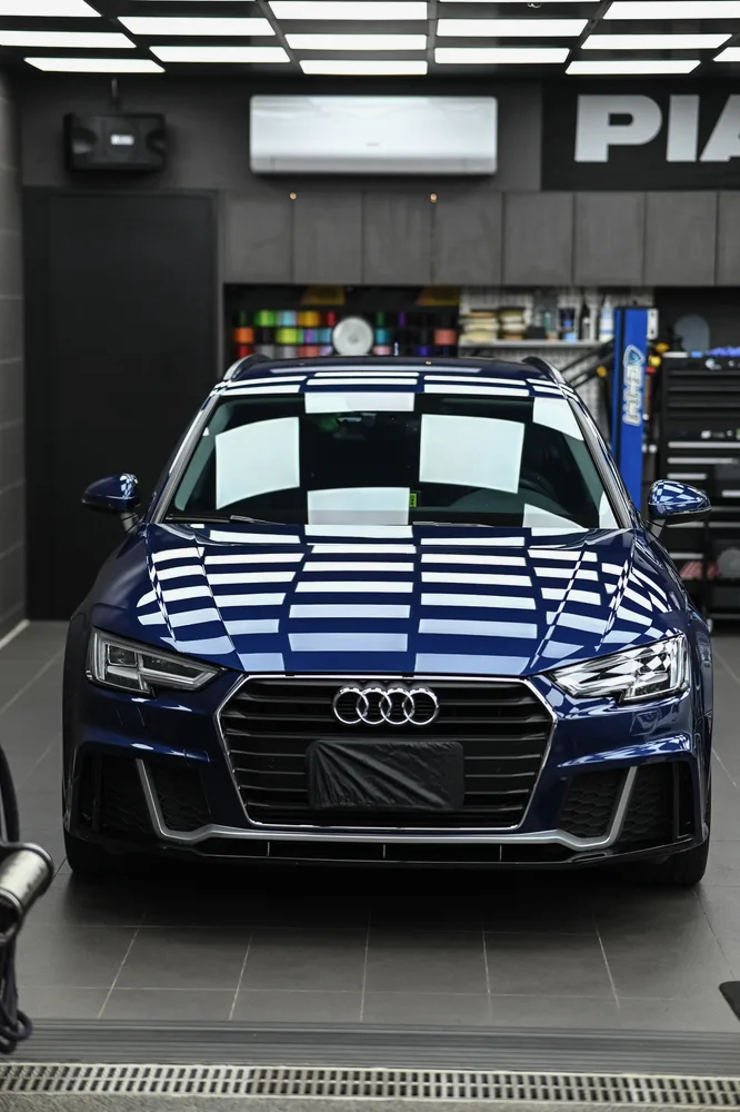 鍍膜完工的深藍色 Audi A4 正面停放於施工區，引擎蓋與水箱護罩映出整排燈條，誠美車體美容