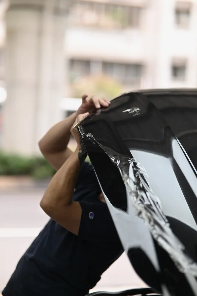 黑色 Ford Mustang 引擎蓋，技師自前緣掀起老化的迎風面保護膜