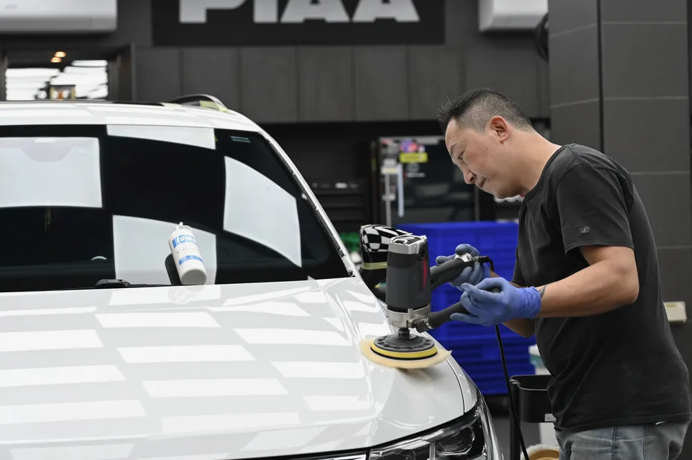 技師以拋光機處理白色休旅車引擎蓋，車頭在燈光下映出格紋倒影，誠美車體美容