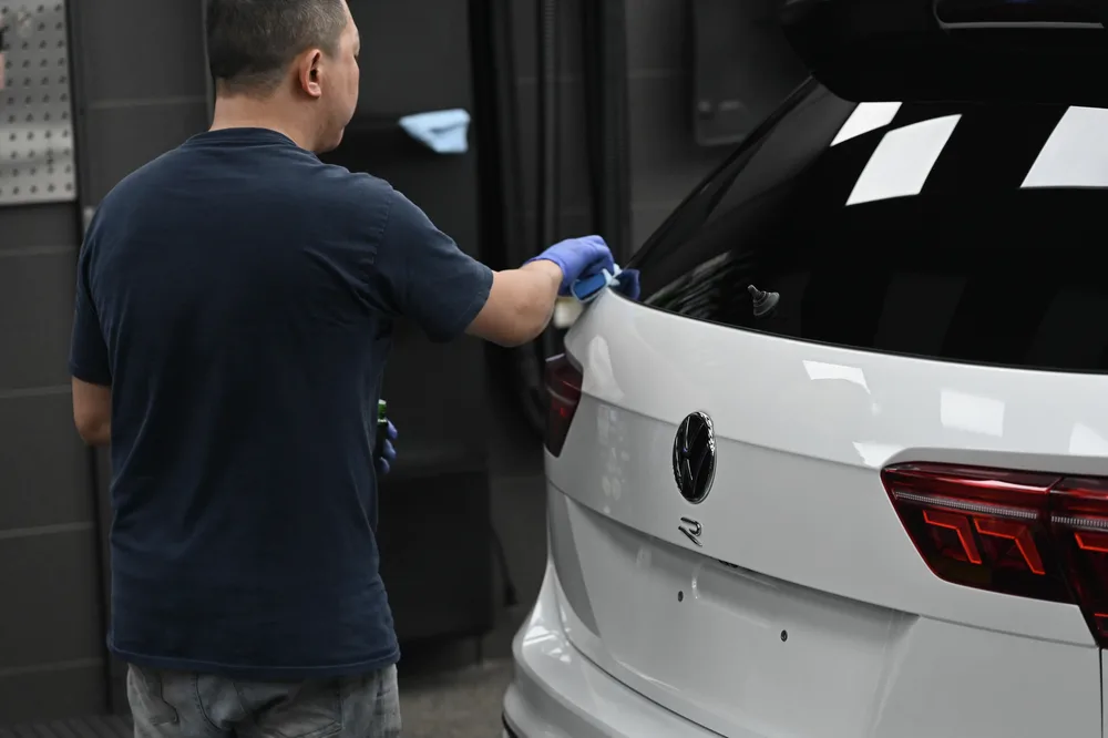 技師站在車尾以施工塊將鍍膜推上尾門上緣與後擋玻璃交界