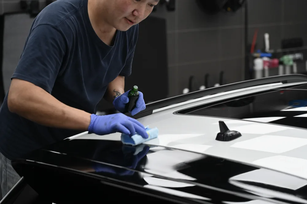 技師俯身在車頂大面積塗佈，車頂映出黑白格紋燈光