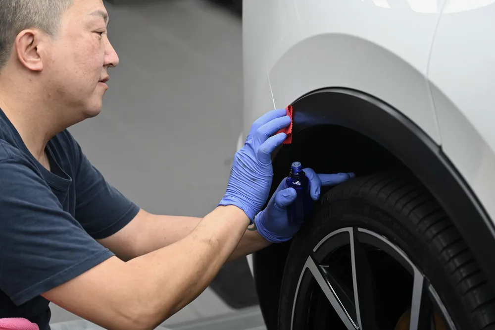 蹲姿於車側作業，海綿貼著輪拱下緣塑料逐段上劑