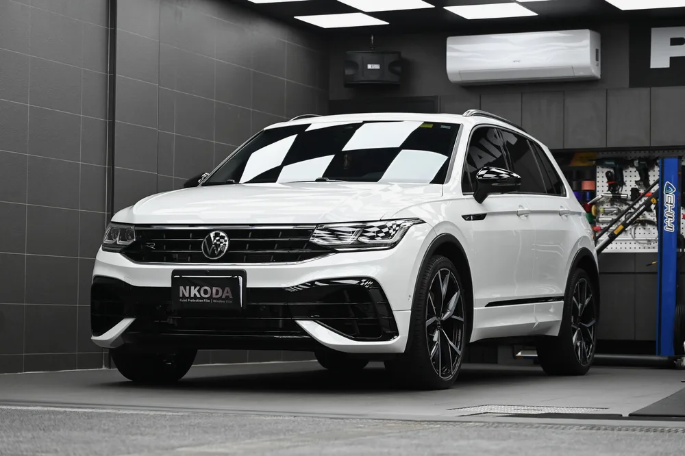 白色 Volkswagen Tiguan 完成車頭迎風面透明保護膜包覆後，停於施工棚內的左前四十五度全車樣貌，誠美車體美容