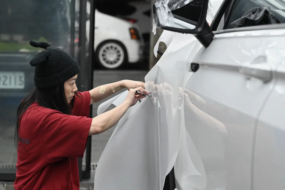 施工人員拉開整片保護膜，準備包覆車側前門鈑面