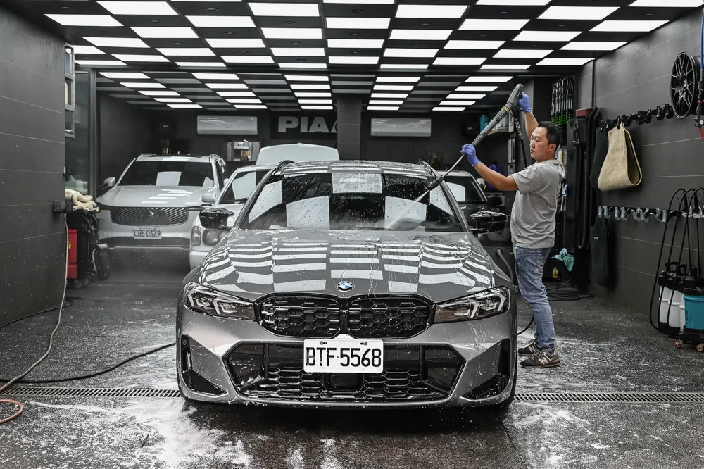 技師在施工區內以高壓水槍沖洗車頭與前保桿，地面積水映出車身