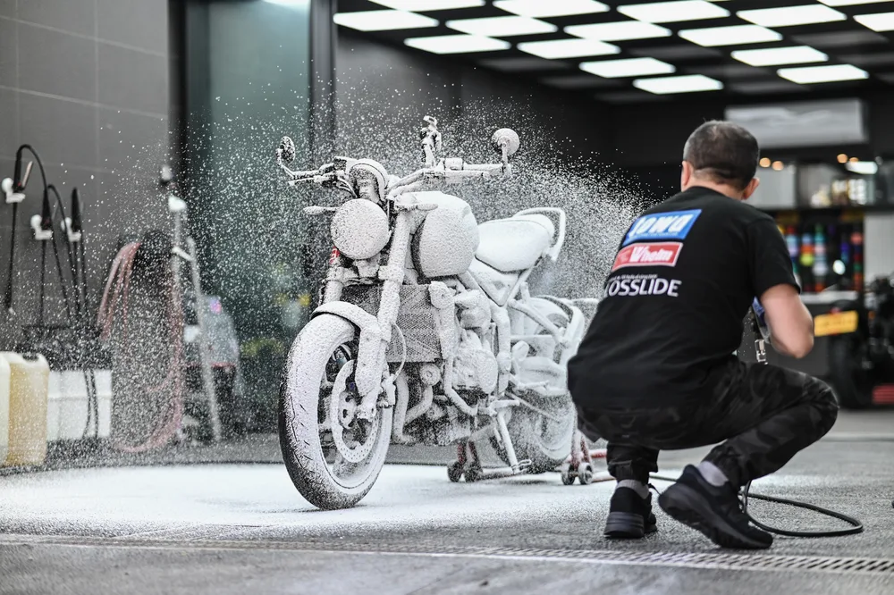 技師以雪泡覆蓋整台 Triumph 重機車身與輪圈,進行鍍膜前的洗車除塵